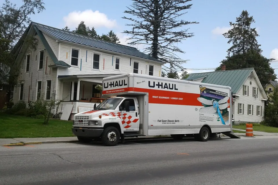 U-Haul moving truck in front of white house and trees